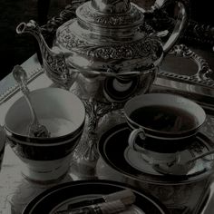 an ornate silver tea set with two cups and saucers next to a plate on a table