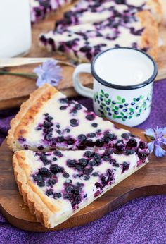 two slices of blueberry cheesecake on a cutting board with a cup of milk