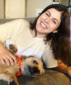 a woman sitting on a couch petting a small brown dog with an orange collar