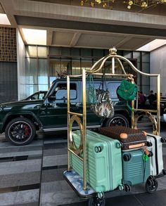 a green truck with luggage on wheels in front of a hotel lobby area and two other vehicles behind it