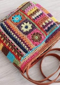 a multicolored crocheted bag sitting on top of a white table next to a brown strap