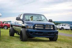 two large trucks parked next to each other on a grass covered field with cars in the background