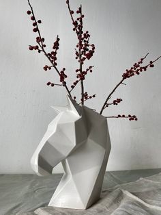 a white vase with red berries in it on a table next to a gray wall