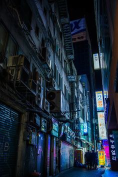 an alley at night with neon signs on the buildings and people walking down the street