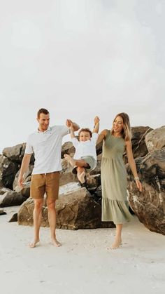 a man, woman and child are standing on the beach with their arms in the air