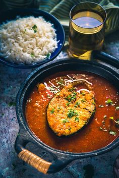 a pan filled with food next to rice and a glass of beer on a table