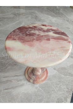 a round marble table with pink and white veining on the top, sitting on a marble pedestal