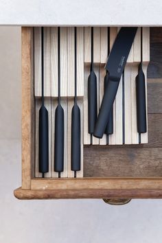 a wooden box with several black knives in it and a knife holder on the side