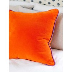 an orange pillow with purple piping on it sitting on a white bed in a bedroom