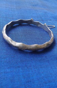 This awesome bangle bracelet is silver, markings inside 925.  It is scalloped and has ingraving throughout that looks tribal to me.  I have had this bracelet since the 80's, but do not hardly ever wear bracelets unless they are made just for me by a child for example.  The lock is somewhat loose, but does have security chain, so it will never fall and get lost.  I have not polished it, but let the patina set in. Ornate Sterling Silver Hallmarked Bangle, Ornate Hallmarked Sterling Silver Bangle Bracelet, Ornate Hallmarked Sterling Silver Bangle, Antique Stamped 925 Silver Bangle, Silver Bangle Stamped 925, Ornate Stamped Bangle Bracelet, Carved Sterling Silver Bracelets, Antique Sterling Silver Bracelet Stamped 925, Vintage Sterling Silver Bangle, Hallmarked