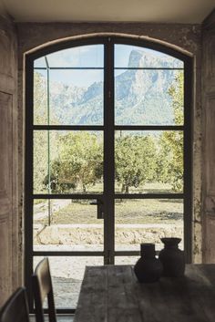 a table with two vases on it in front of an open window that looks out onto the mountains