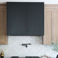 a kitchen with wooden cabinets and white tile backsplash, black range hood over the stove