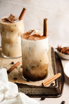 two glasses filled with iced coffee on top of a tray next to cinnamon sticks and spices