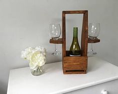 a wine bottle and some glasses on a white table with a flower in a vase