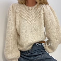 a woman wearing a white sweater and denim skirt sitting on the floor with her hands in her pockets