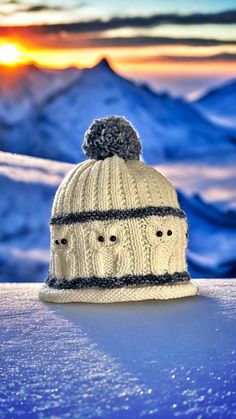 a knitted hat sitting on top of a snow covered slope with mountains in the background