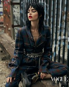 a woman sitting on top of a wooden bench wearing a suit and chain bracelets