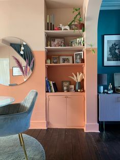 a living room with pink and blue walls, bookshelves and a mirror on the wall