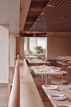 an empty restaurant with wooden tables and white plates on the long table, in front of a large window