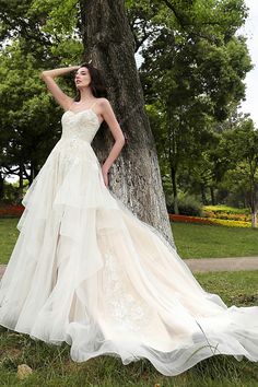 a woman in a wedding dress leaning against a tree