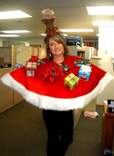 a woman wearing a santa hat and holding presents in an office cubicle with christmas decorations on it