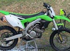 a green and white dirt bike parked on top of a grass covered field with trees in the background