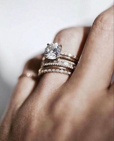 a woman's hand with two wedding rings on her left and the other hand holding an engagement ring