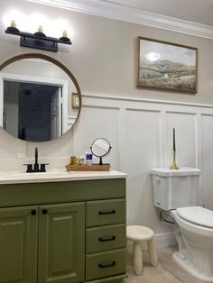 a bathroom with green cabinets and a white toilet next to a mirror on the wall