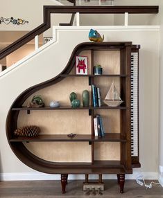 a piano shaped bookcase in the corner of a living room with stairs and bookshelves