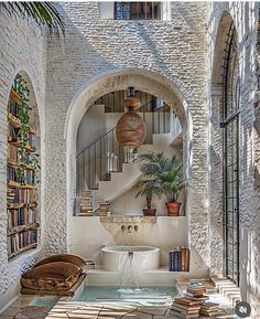 an indoor fountain in the middle of a room with bookshelves and potted plants