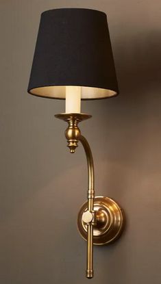 a wall light with a black shade on it's side and a white lamp in the corner