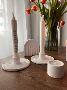 three candles and two vases on a table with tulips in the background