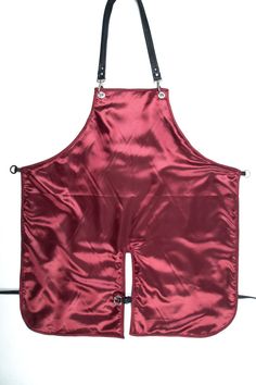 a red apron is hanging on a white wall and it has black straps around the neck