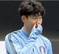 a young man wearing a blue shirt and holding his hand up to his face while looking at something