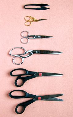 five pairs of scissors lined up on a pink surface