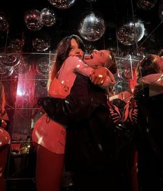 two women hugging each other in front of mirrored balls and disco ball decorations on the wall