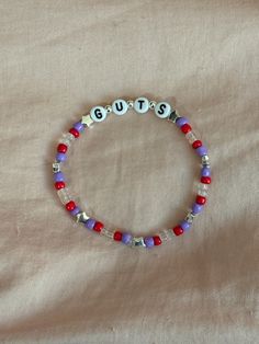 A hand-crafted glass bead friendship bracelet highlighting Olivia Rodrigo's album, GUTS! A simple and cute way to show off your favorite song or a great concert accessory!  This bracelet is made with Czech glass beads, plastic letter beads, plastic spacer beads, and is on an elastic thread measured at about 10 inches in length for a relaxed/loose fit. If you would like the bracelet you order to be smaller or larger, please leave the requested size in inches in the personalization box!  All bracelets are made to order and are typically shipped out within 1-3 business days unless otherwise stated. Olivia Friendship Bracelet, Guts Friendship Bracelet, Olivia Rodrigo Friendship Bracelet, Olivia Rodrigo Bracelets, Friendship Bracelets Simple, Olivia Rodrigo Bracelet, Bead Friendship Bracelet, Beaded Braclets, Guts Tour