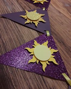 three purple and gold paper sun decorations on a wooden table