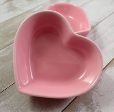 two pink heart shaped bowls sitting on top of a wooden floor