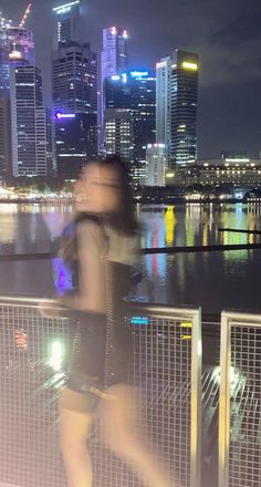 a blurry photo of a woman walking on a bridge over water with city lights in the background