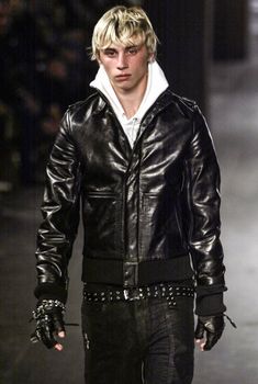 a man in black leather jacket walking down a runway