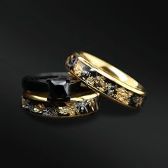 two wedding rings with black and gold designs on the sides, one has a stone embedded in it