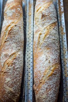 two loaves of bread sitting on top of a metal pan covered in powdered sugar