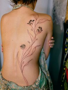 the back of a woman's body with flowers tattooed on her upper and lower back