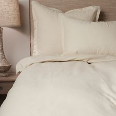 a bed with white sheets and pillows on top of it next to a night stand