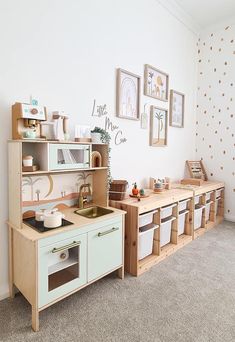 a child's play kitchen with wooden cabinets and drawers in a white walled room