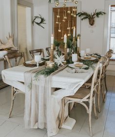 a dining room table set for christmas with candles and greenery on the table runner