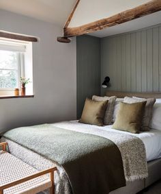 a bed sitting under a window next to a wooden table and chair in a bedroom