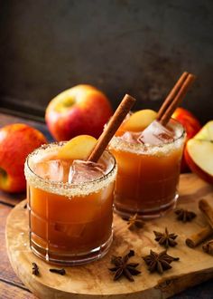 two glasses filled with apple cider on top of a cutting board