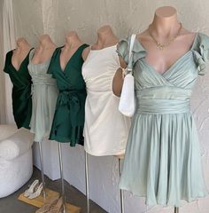 three dresses on mannequins in front of a white wall and one is green